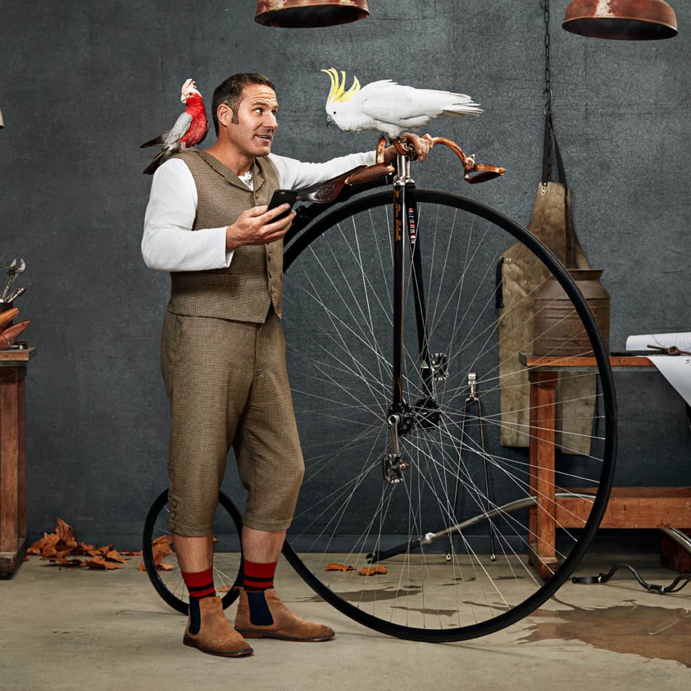 Dan Blowell stands with his penny-farthing bicycle, where a cockatoo bird randomly sits on the handles.